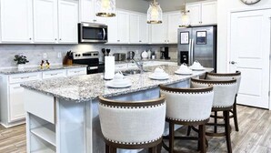 A modern kitchen with white cabinets, a granite countertop, a stainless steel refrigerator, and pendant lighting. - Scifi Theater Amazing Theme 7 Bed Pool Home 7 Bedroom Home (Davenport)