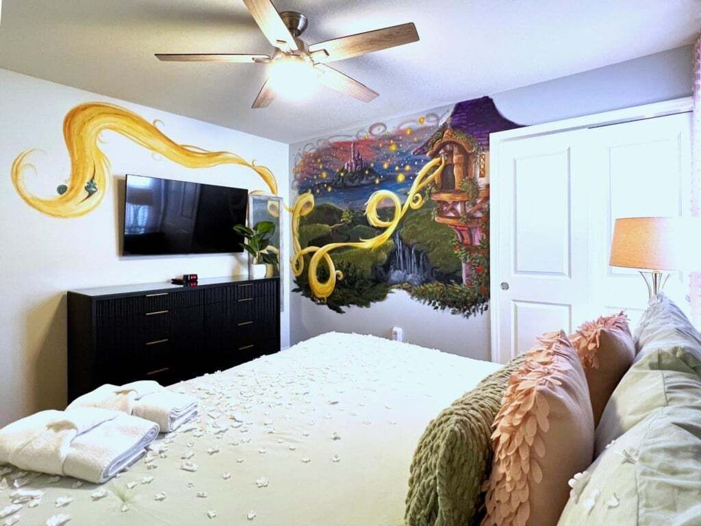 A bedroom with a bed, a television, a dresser, and a mural on the wall.