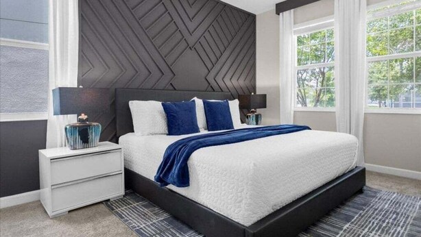 A modern bedroom with a large bed, dark headboard, white nightstands, and a view of greenery through large windows. - Star Wars & More Large Private Pool Lanai Home! 6 Bedroom Villa (Davenport)