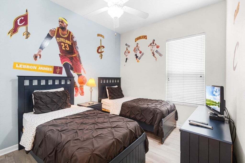 Ett sovrum med två sängar, en takfläkt, en tv och inredning med Cleveland Cavaliers-tema.