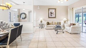 A spacious living area with a dining table, two sofas, a ceiling fan, and a large window. - 4 Bed Pool Home, Pool Table & More 4 Bedroom Villa (Davenport)