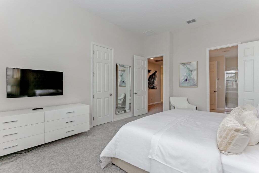 A bedroom with a large bed, a TV mounted on the wall, a dresser, and a closet with sliding doors.
