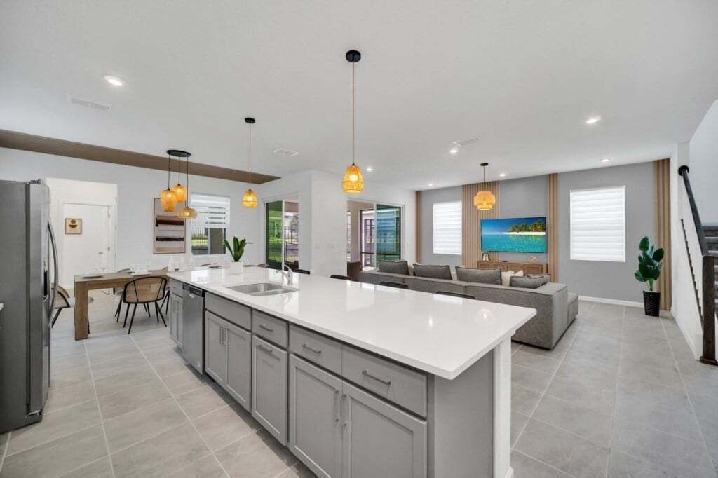 A modern kitchen with a central island, pendant lighting, and a dining area with a table and chairs.