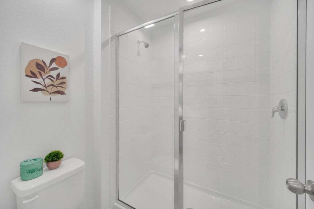 Une salle de bain moderne avec une douche à l’italienne en verre, des toilettes agrémentées d’une petite plante en pot et une œuvre d’art accrochée au mur.