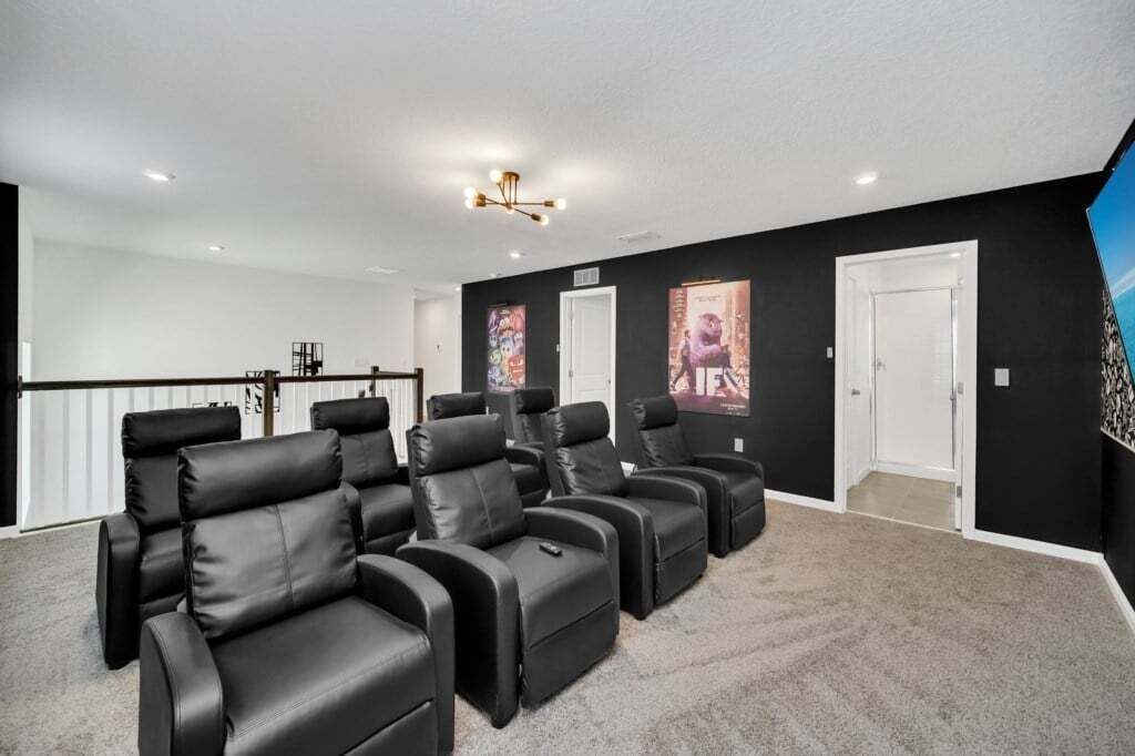 Une salle de cinéma privée avec des fauteuils en cuir noir inclinables, un sol recouvert de moquette et un grand téléviseur à écran plat fixé au mur.