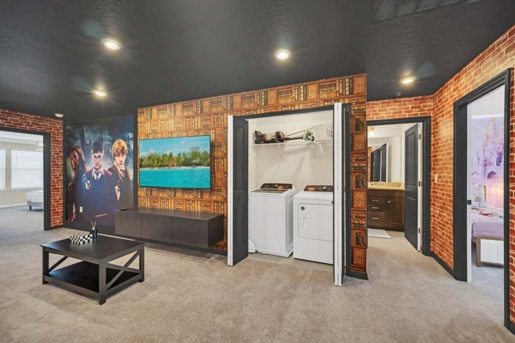 Una habitación con pared de ladrillo, un cuadro, lavadora y cama.