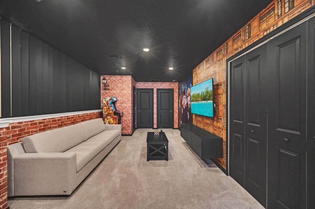 A modern living room with a brick accent wall, a beige sofa, a black coffee table, and a television mounted on the wall.
