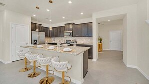A modern kitchen with a central island, bar stools, and stainless steel appliances. - Luxury Home With Splash Pool 5 Bed Townhome! 5 Bedroom Townhouse (Clermont)