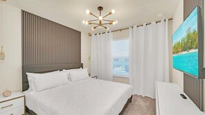 A hotel room with a large bed, a TV, a bedside table, and a window with curtains. - Luxury Home With Splash Pool 5 Bed Townhome! 5 Bedroom Townhouse (Clermont)