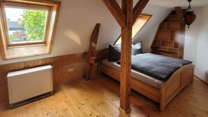 A bedroom with a sloped ceiling, wooden beams, a bed, a window, and a radiator.