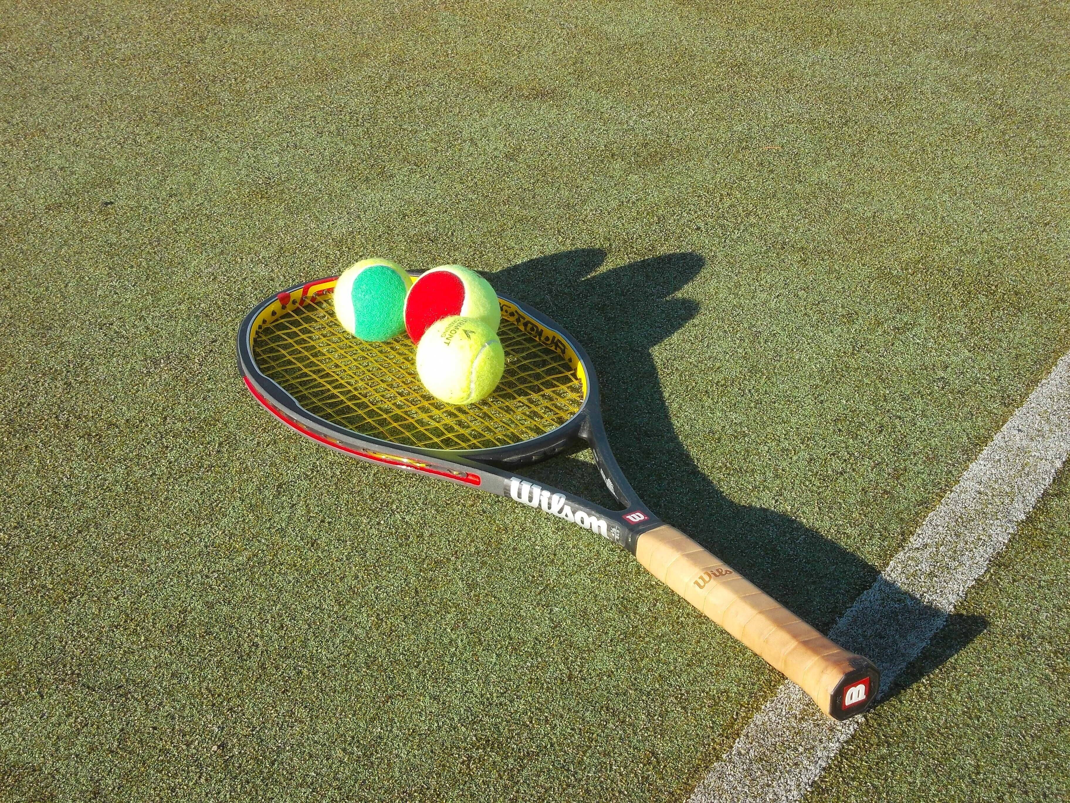 Tennismaila ja kolme tennispalloa vihreällä alustalla.