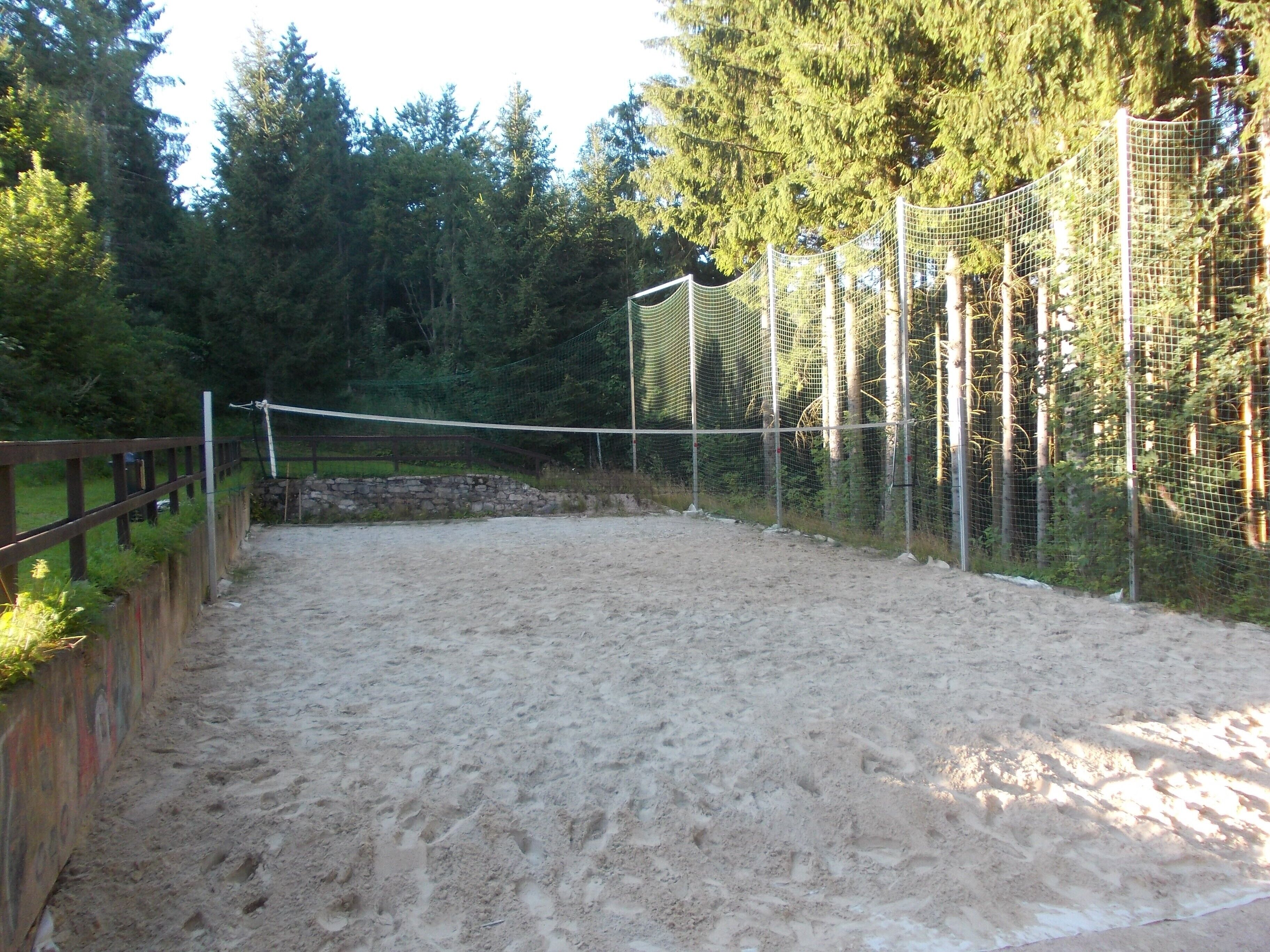 A sandy volleyball court with a net, surrounded by a wooden fence and trees.