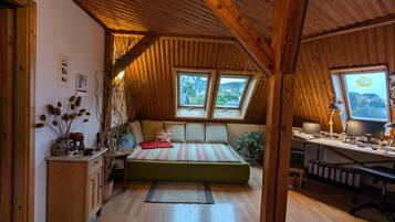 Ein gemütliches Schlafzimmer im Dachgeschoss mit schrägen Wänden, einem Bett, einem Schreibtisch und Blick ins Freie.