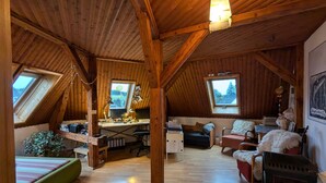 A wooden interior with a loft bedroom, a desk, and a sofa.