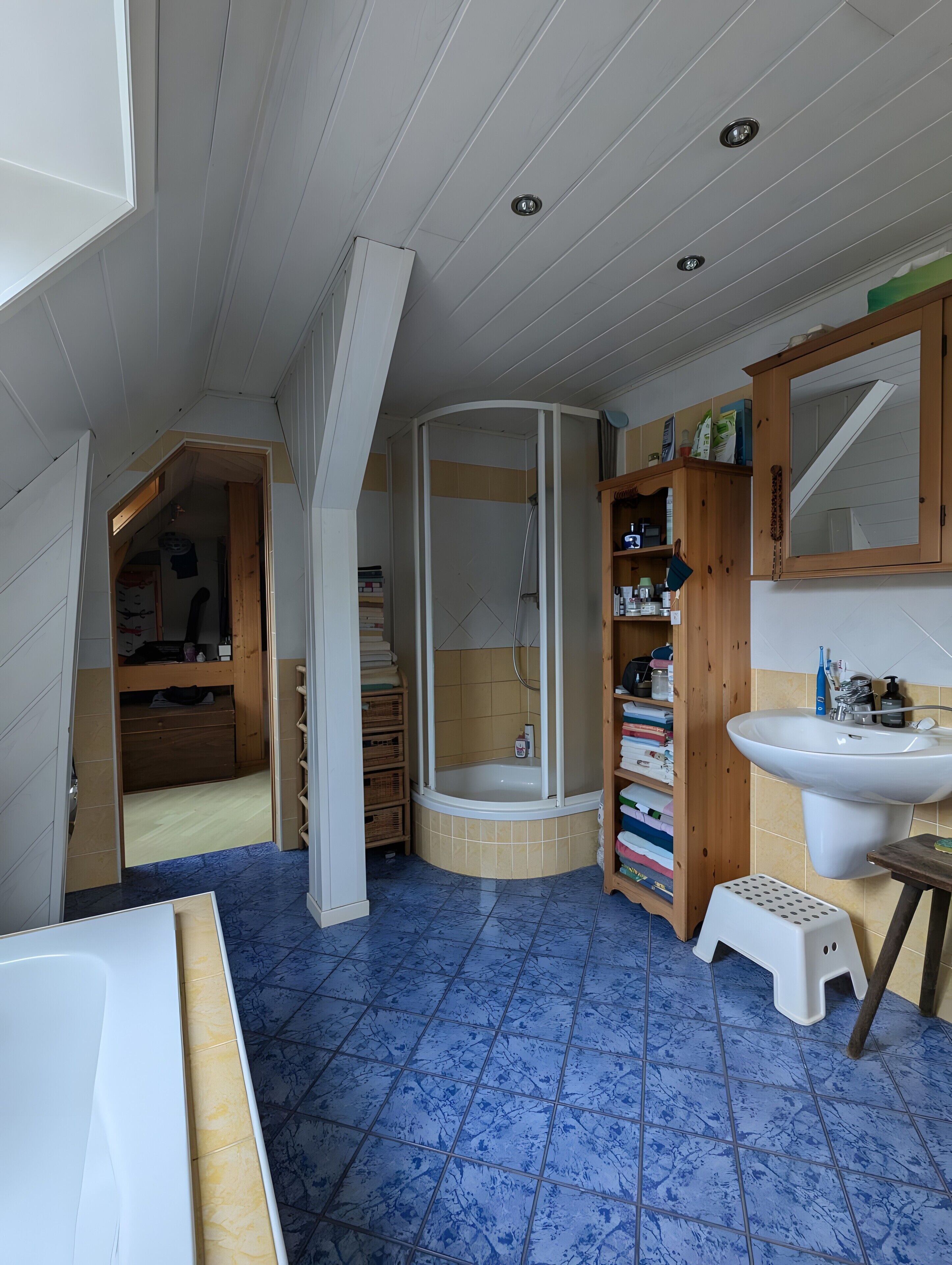 A bathroom with a bathtub, a sink, a shower, and a wooden shelving unit.