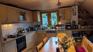 A kitchen with wooden cabinets, a dining table with chairs, a vase with flowers, and a hanging lamp.