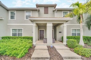 A two-story building with a covered entrance, a door, and a small porch area. - Retreat & Relax Screened In Pool Home Kid Rooms 4 Bedroom Townhouse (Kissimmee)