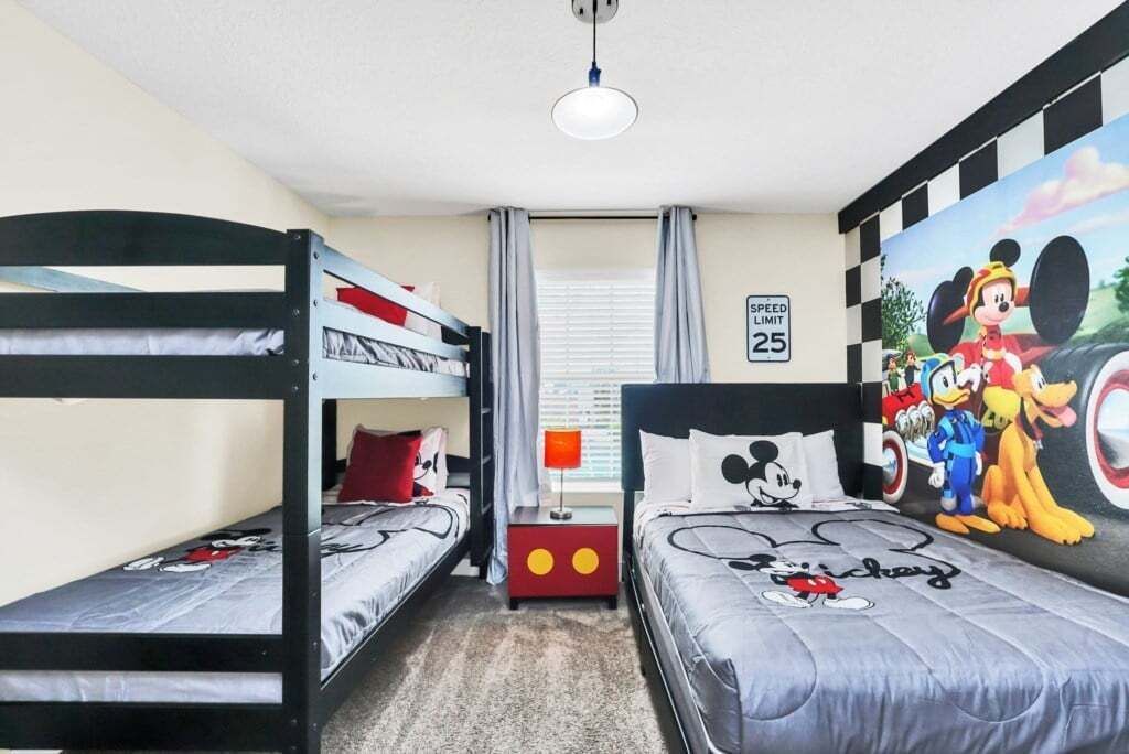 A room with bunk beds, a Mickey Mouse themed bedspread, a speed limit sign, and a mural of Disney characters.