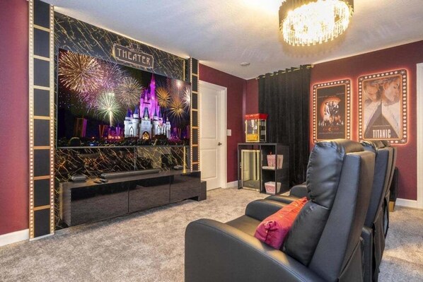 A home theater room with a large screen displaying fireworks, a plush black sofa, and a red curtain. - The Most Stunning Home With Everything You Want! 8 Bedroom Villa (Davenport)