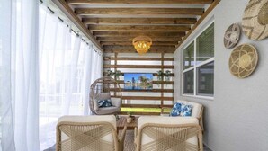 Un'accogliente area salotto con mobili in vimini, soffitto in legno e vista sulla città attraverso una finestra.