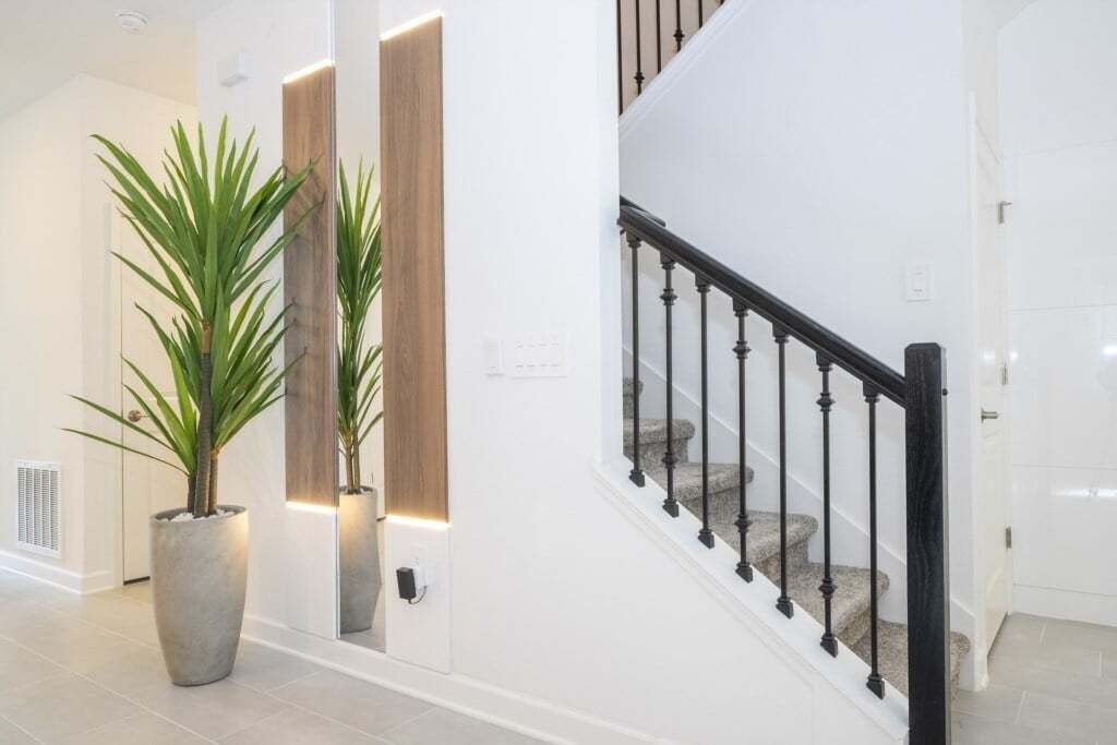 A staircase with black balusters and a handrail, leading to a landing with a light switch and a wall-mounted light fixture.