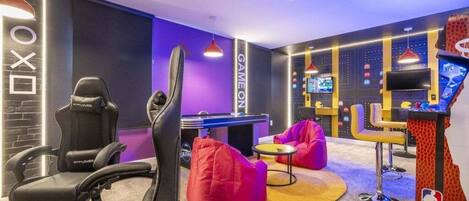 A gaming room with a racing game setup, bean bag chairs, and a pool table.