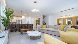 Un soggiorno moderno con divano, tavolino e poltrone. Si intravede una zona cucina sullo sfondo.