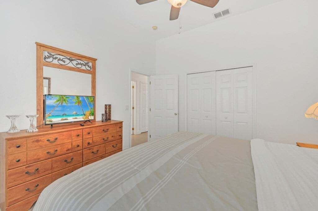 Une chambre à coucher avec un lit, une commode, un miroir et un ventilateur de plafond.