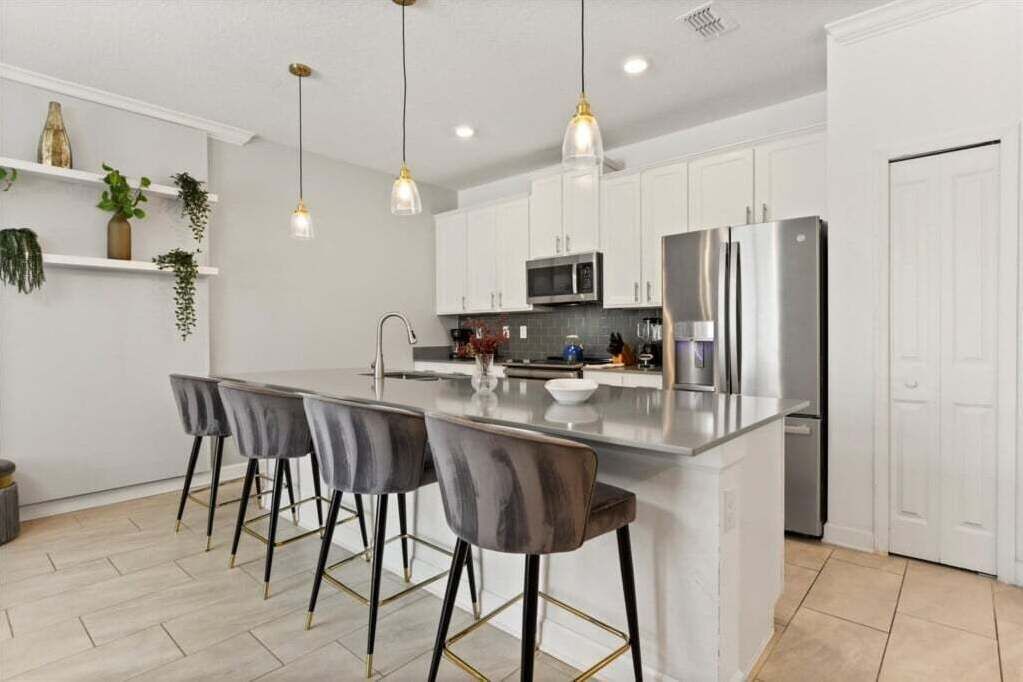 A modern kitchen with white cabinets, a stainless steel refrigerator, a microwave, and a bar area with stools.