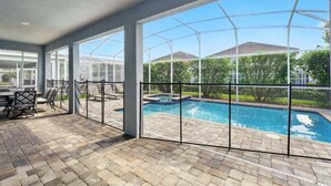 Ein überdachter Patio-Bereich mit Pool, Gartenmöbeln und großen Fenstern.