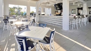 An outdoor dining area with tables and chairs, a bar area with a counter, and a view of a water park in the background. - Stunning 4 Bed Townhome Pool & Waterpark 4 Bedroom Townhouse (Davenport)