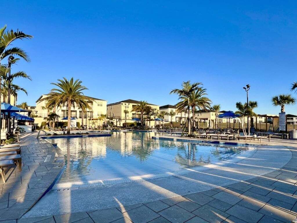 A swimming pool area with palm trees, lounge chairs, and a building in the background.