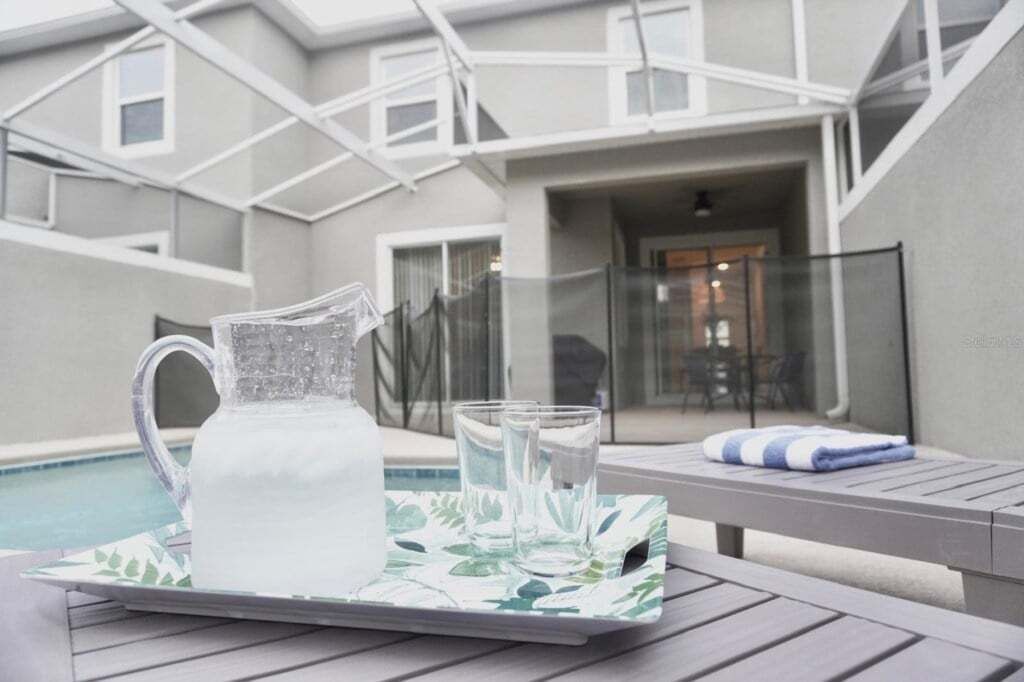 A patio area with a table set for two, a pitcher, and glasses on a tray.