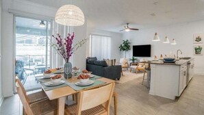 A modern kitchen with a central island, a dining area with a table set for four, and a living room with a sofa and a TV. - Stunning 4 Bed Townhome Pool & Waterpark 4 Bedroom Townhouse (Davenport)