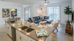 A modern kitchen with a central island, stainless steel appliances, and a dining area with a table and chairs. - Stunning 4 Bed Townhome Pool & Waterpark 4 Bedroom Townhouse (Davenport)