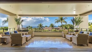A covered outdoor seating area with wicker furniture and a view of the ocean and palm trees. - Wailea Beach Villa K207 2 Bedroom Villa (Kihei)