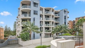 A multi-story residential building with balconies, a gated entrance, and surrounding greenery.