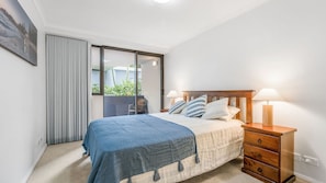 A bedroom with a bed, bedside tables, a window, and a view of greenery outside.