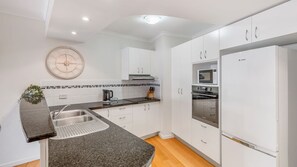 A modern kitchen with white cabinets, a stainless steel sink, a microwave, and an oven.