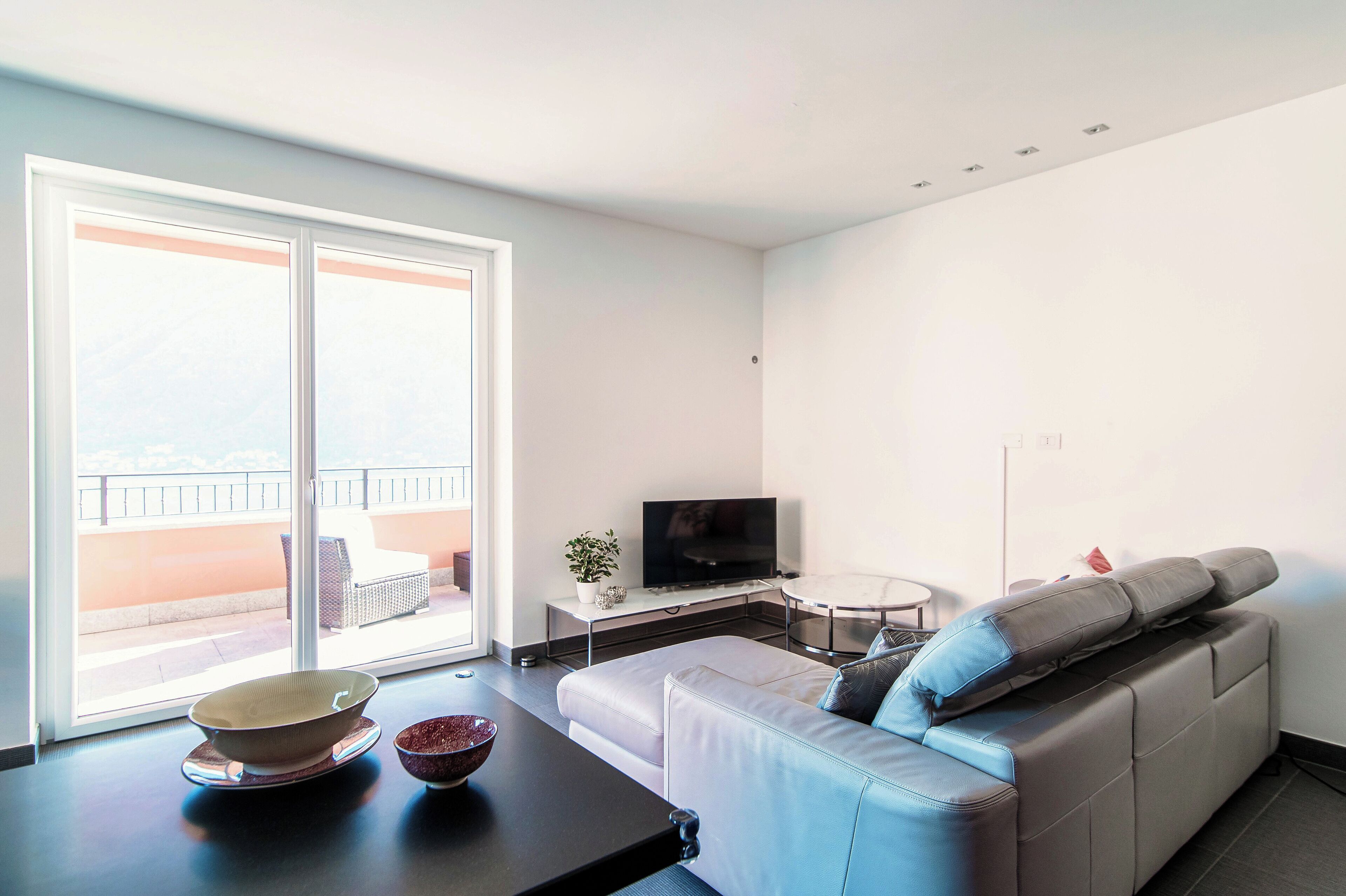 Una sala moderna con un sofá, televisión y vistas al balcón.