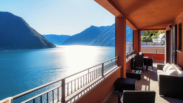 Un balcone con mobili in vimini, vista su un lago e montagne sullo sfondo.
