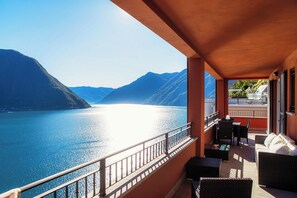 A balcony with wicker furniture, a view of a lake, and mountains in the background. - Rosso Sunset (Colonno)