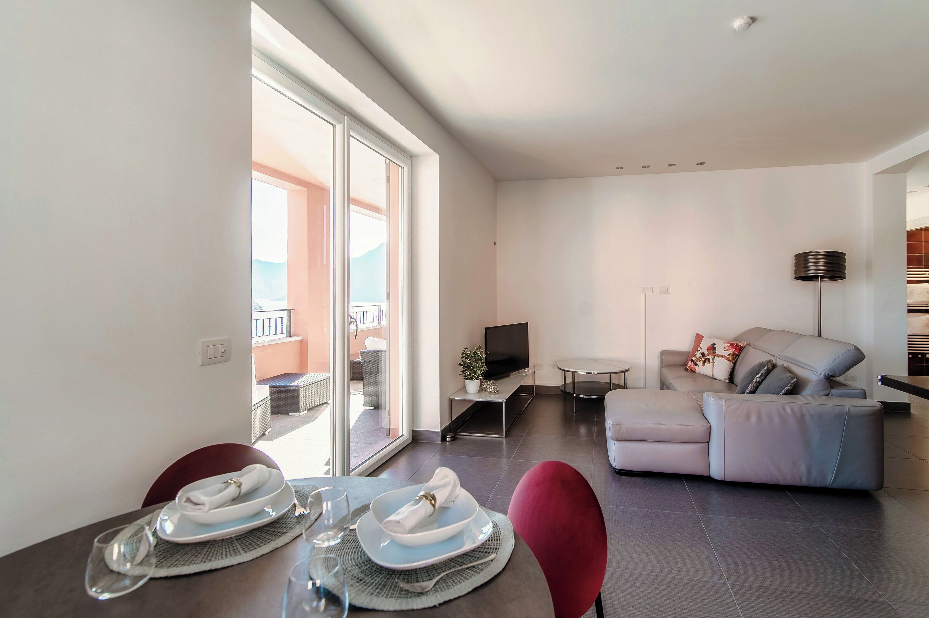 A modern living area with a sofa, a TV on a stand, and a dining table set with plates and glasses.