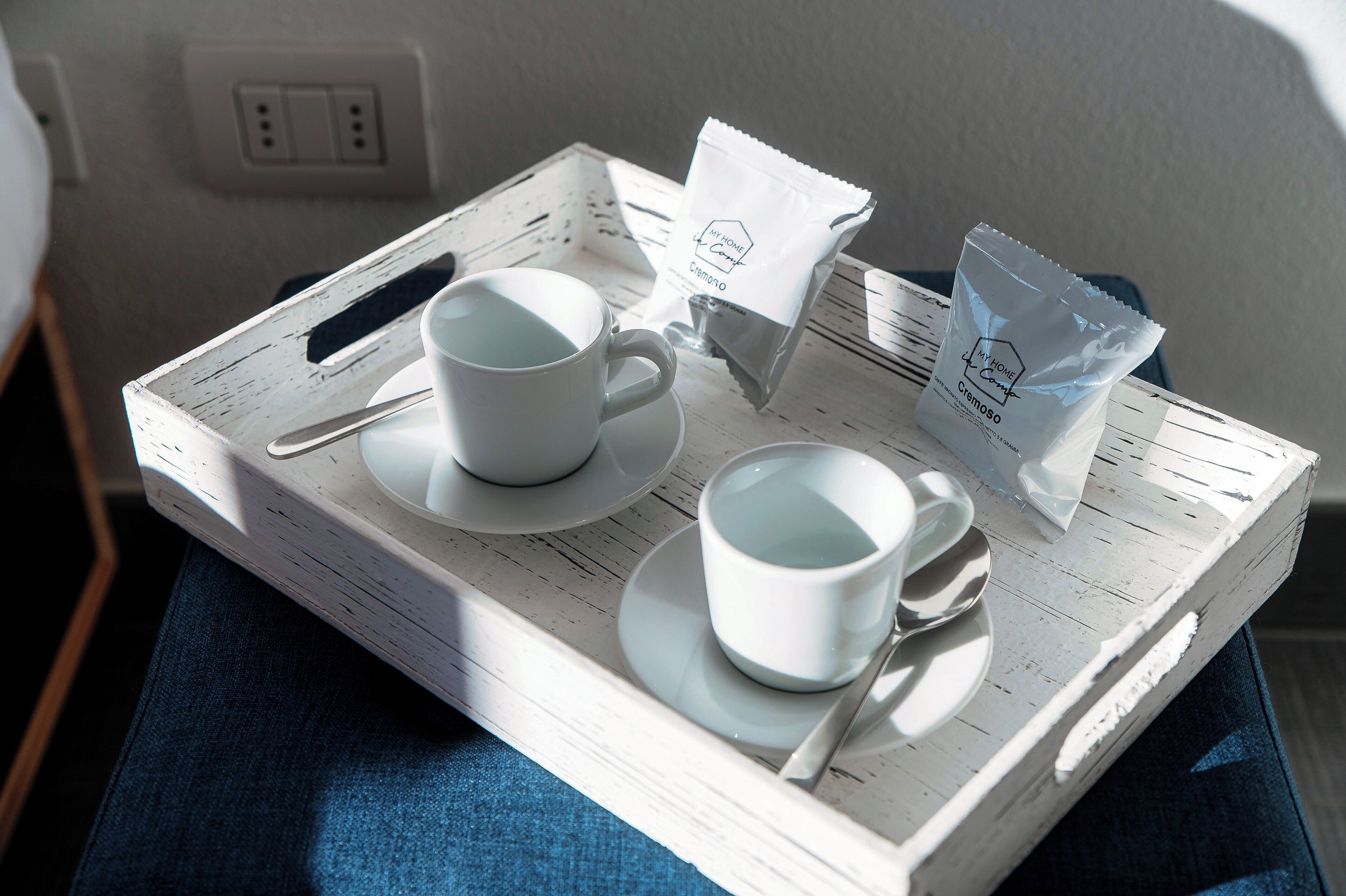 A tray with two white cups, a spoon, and a packet of cremoso tea on a rustic wooden tray.