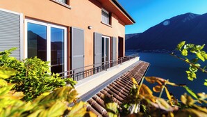 Una casa moderna con ampie finestre, un balcone e vista su un lago e montagne.