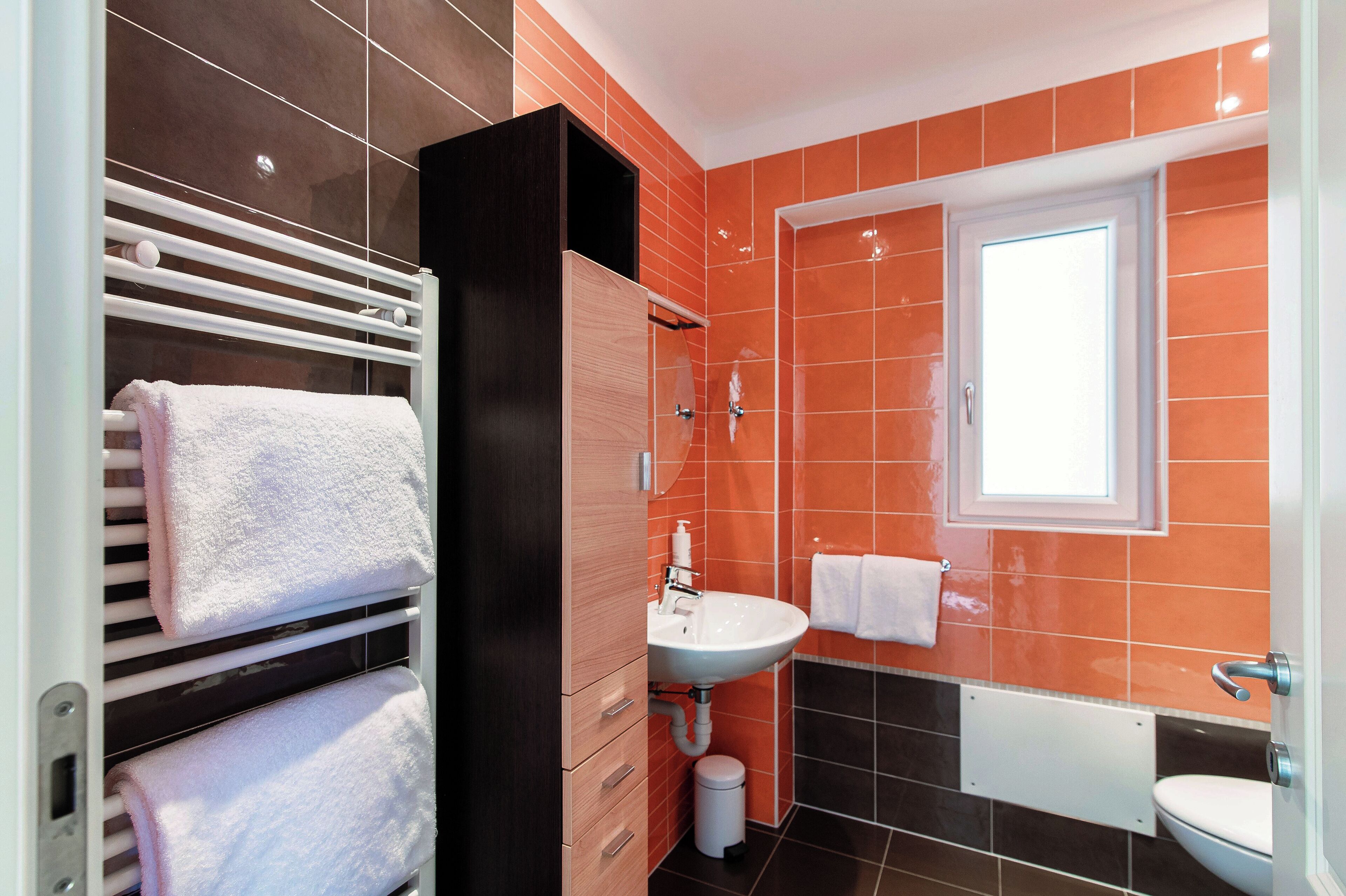 A modern bathroom with a white sink, a toilet, and a towel rack with white towels.