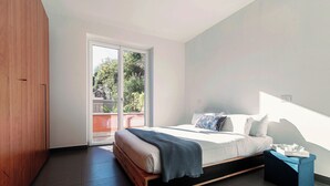 Una camera da letto moderna con un letto grande, un armadio in legno e una porta a vetri scorrevoli che dà su un balcone esterno.
