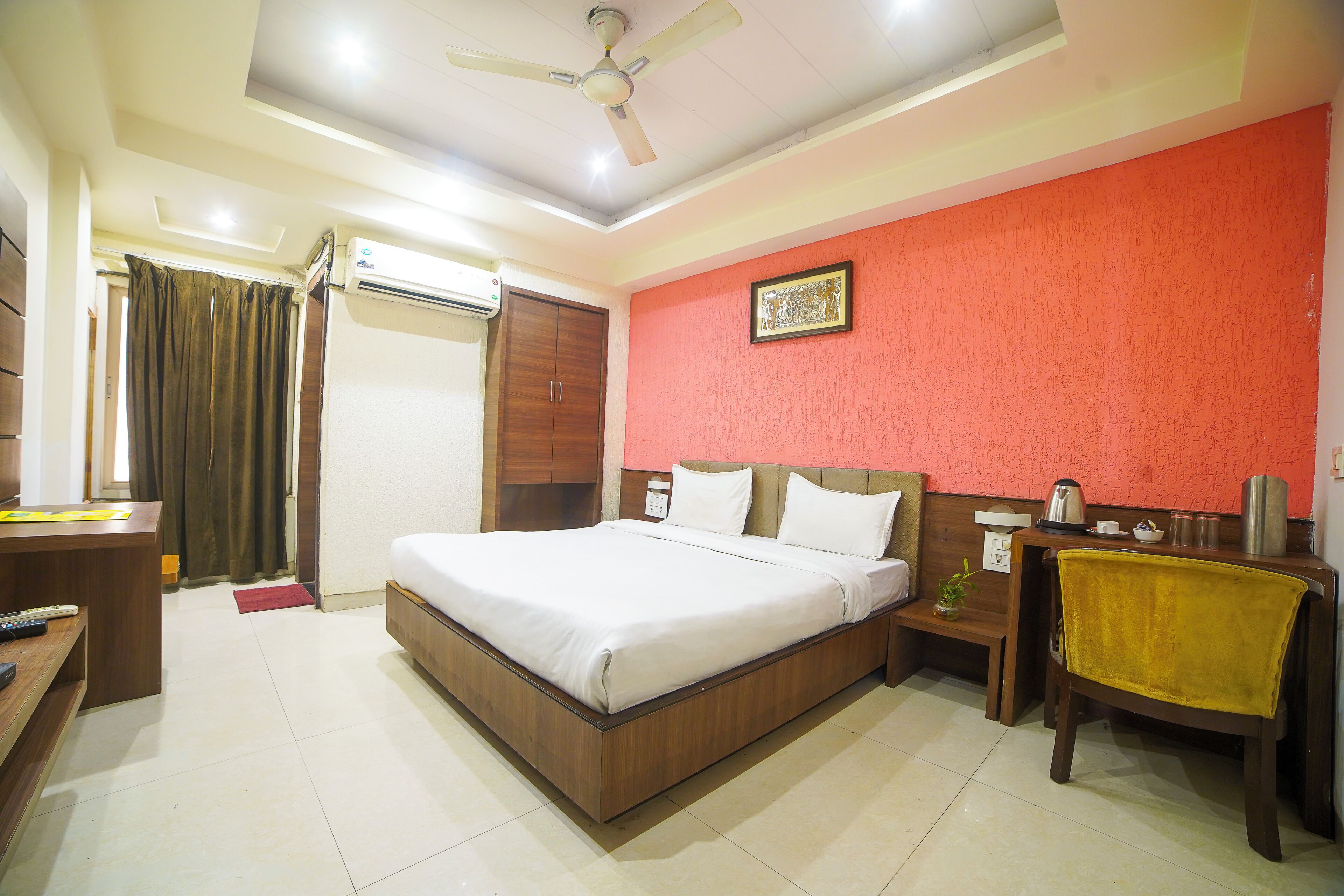 A hotel room with a bed, a desk, a chair, a nightstand, a red wall, and a ceiling fan.