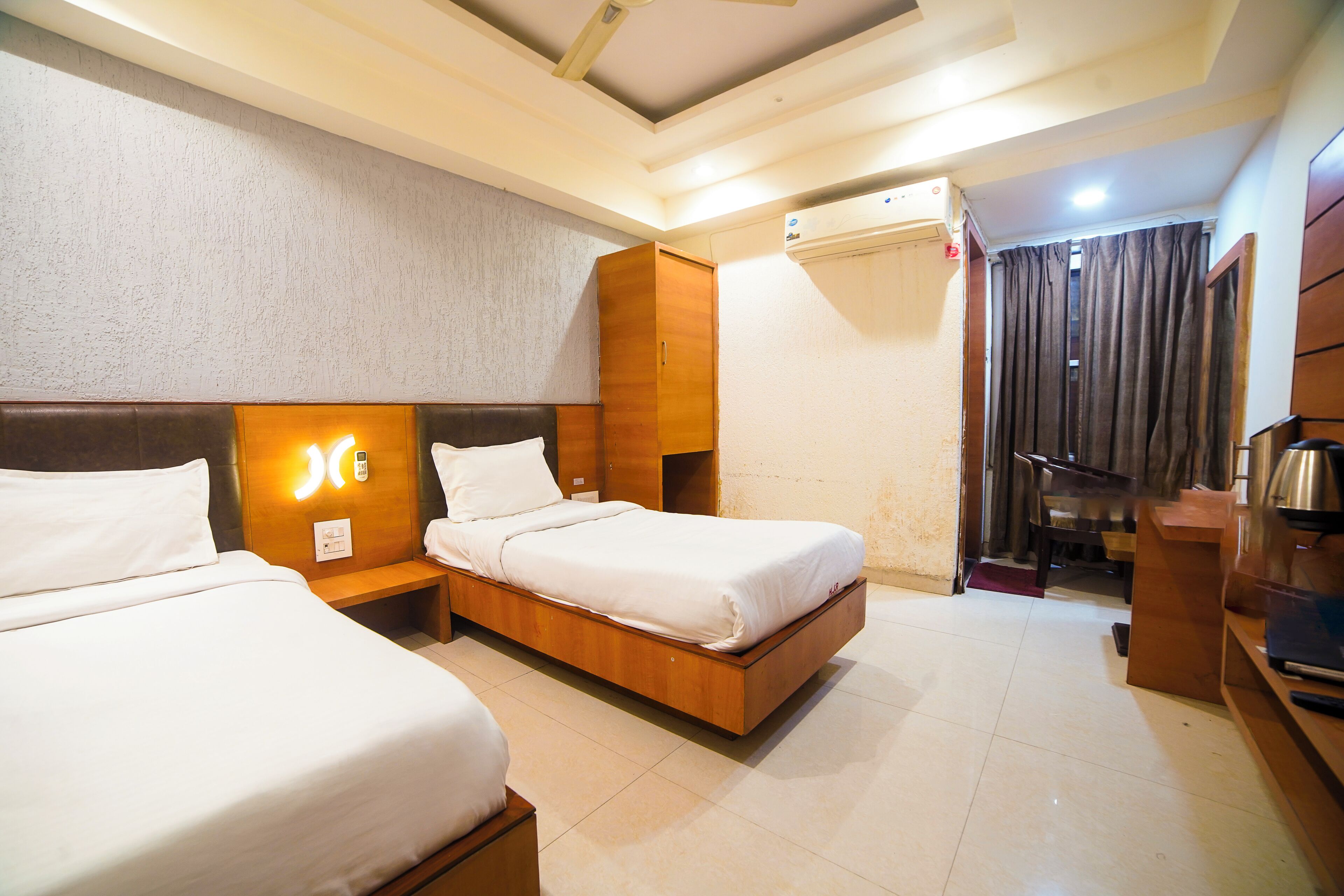 A hotel room with two beds, a wooden headboard, a bedside table with a phone, and a small desk with a kettle.