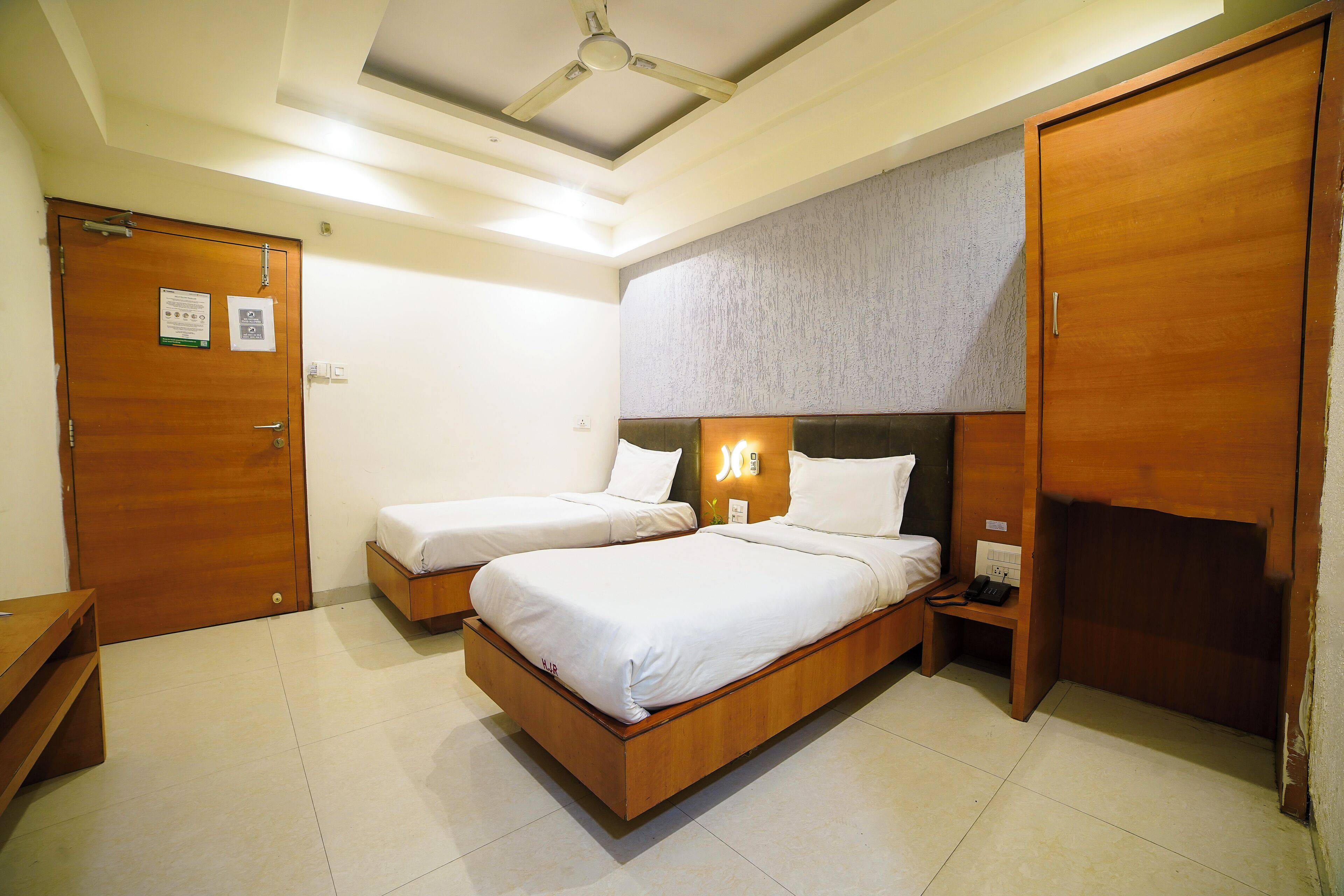 A bedroom with two single beds, a wooden wardrobe, a bedside table with a phone, and a ceiling fan.